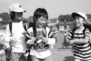 Photograph of three smiling children who seem to be getting along as they walk to or from school.